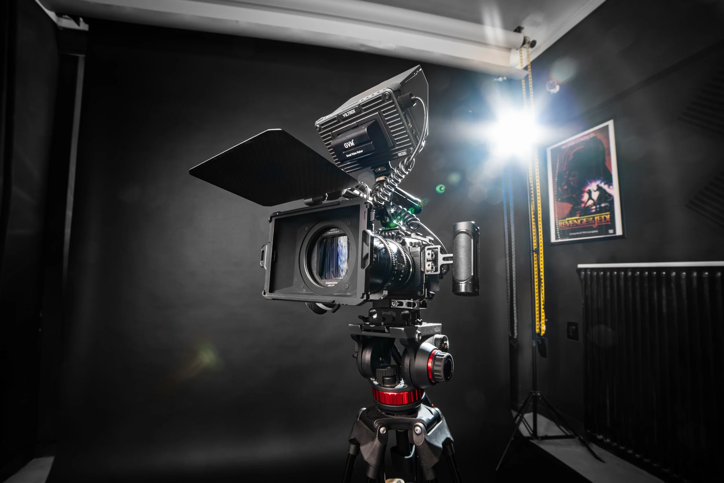 A professional camera mounted on a tripod in a studio, with bright light and a poster on the wall.