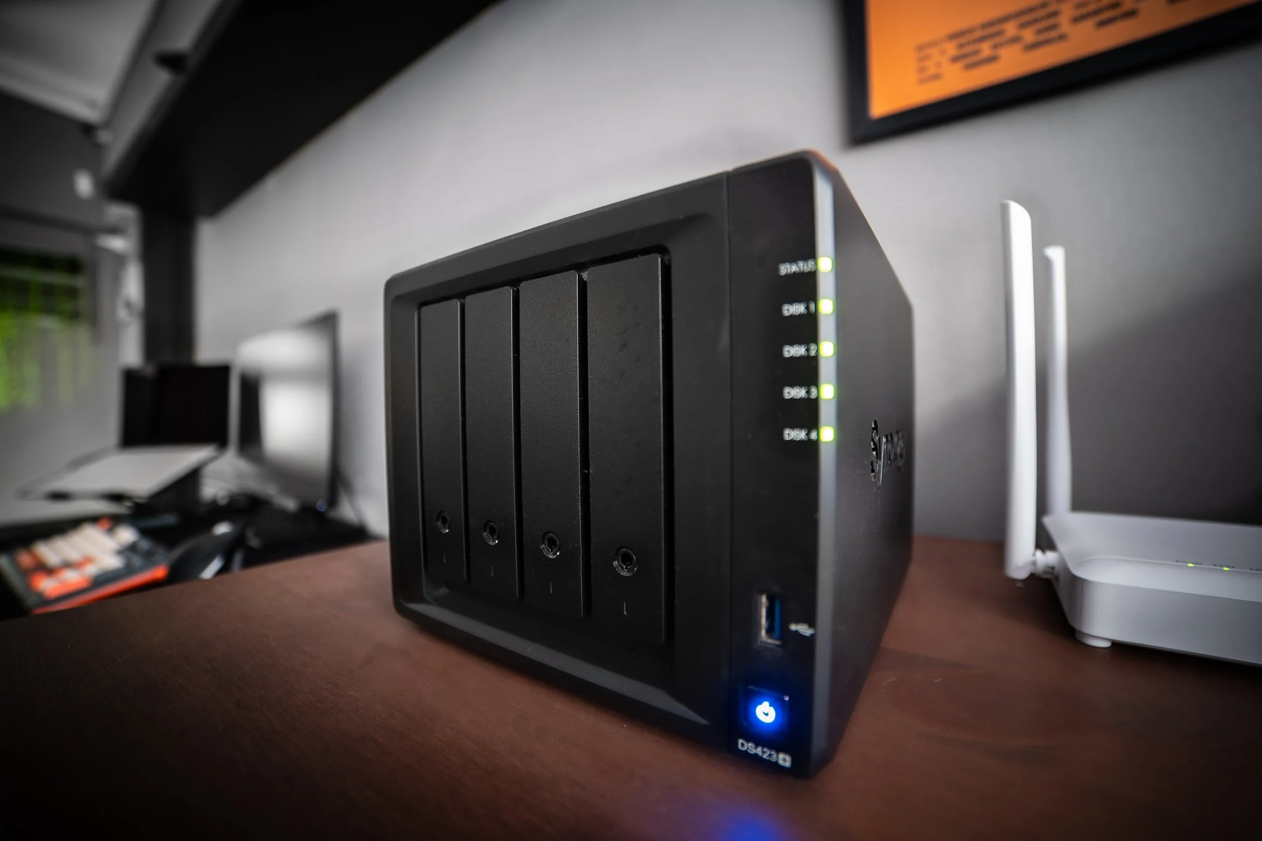 A black network-attached storage (NAS) device with multiple hard drive bays and indicator lights, placed on a wooden desk.