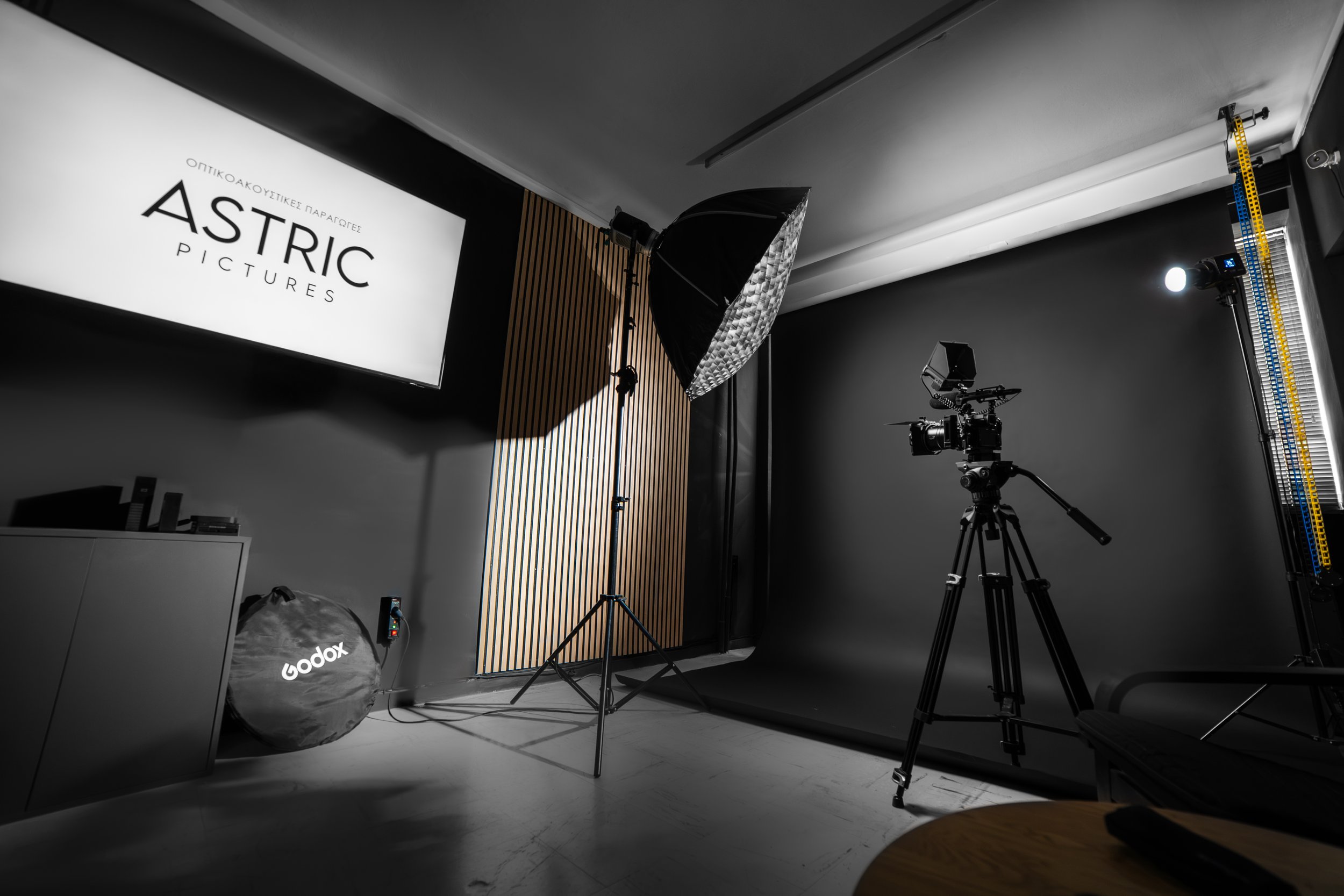 Photography studio setup with professional lighting, a camera on a tripod, and a large screen displaying 'ASTRIC PICTURES' in black and white.