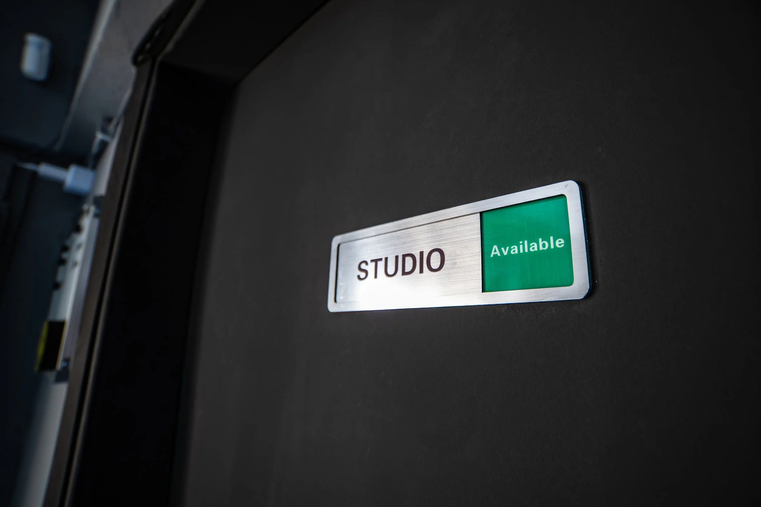A sign on a black door that reads 'STUDIO Available' with a green background on the word 'Available'.