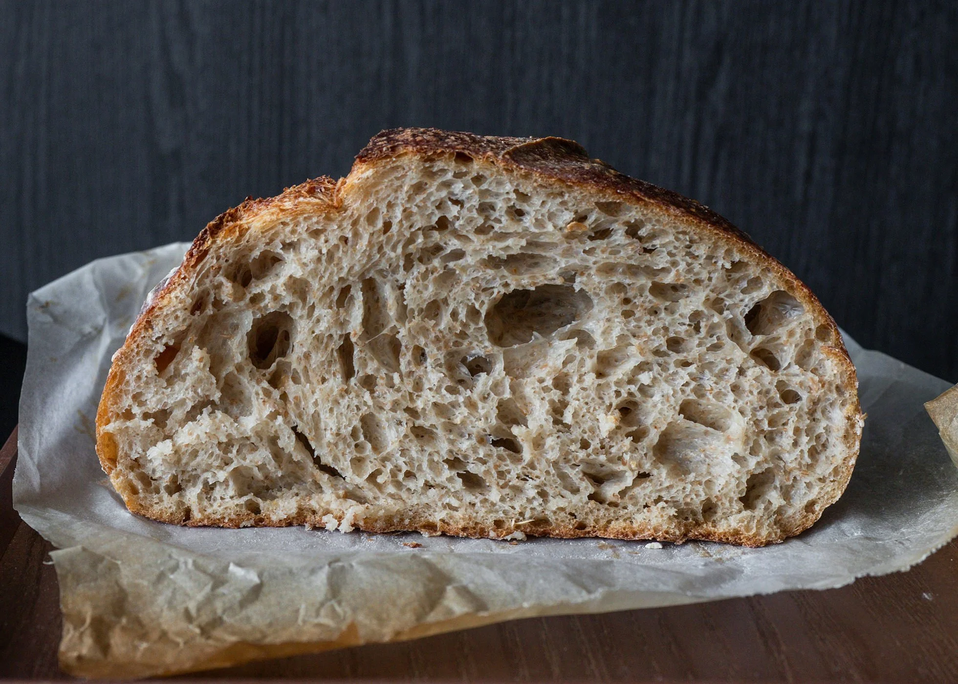 A loaf of sourdough on a chopping board already cut into & showing a variety of sized air bubbles
