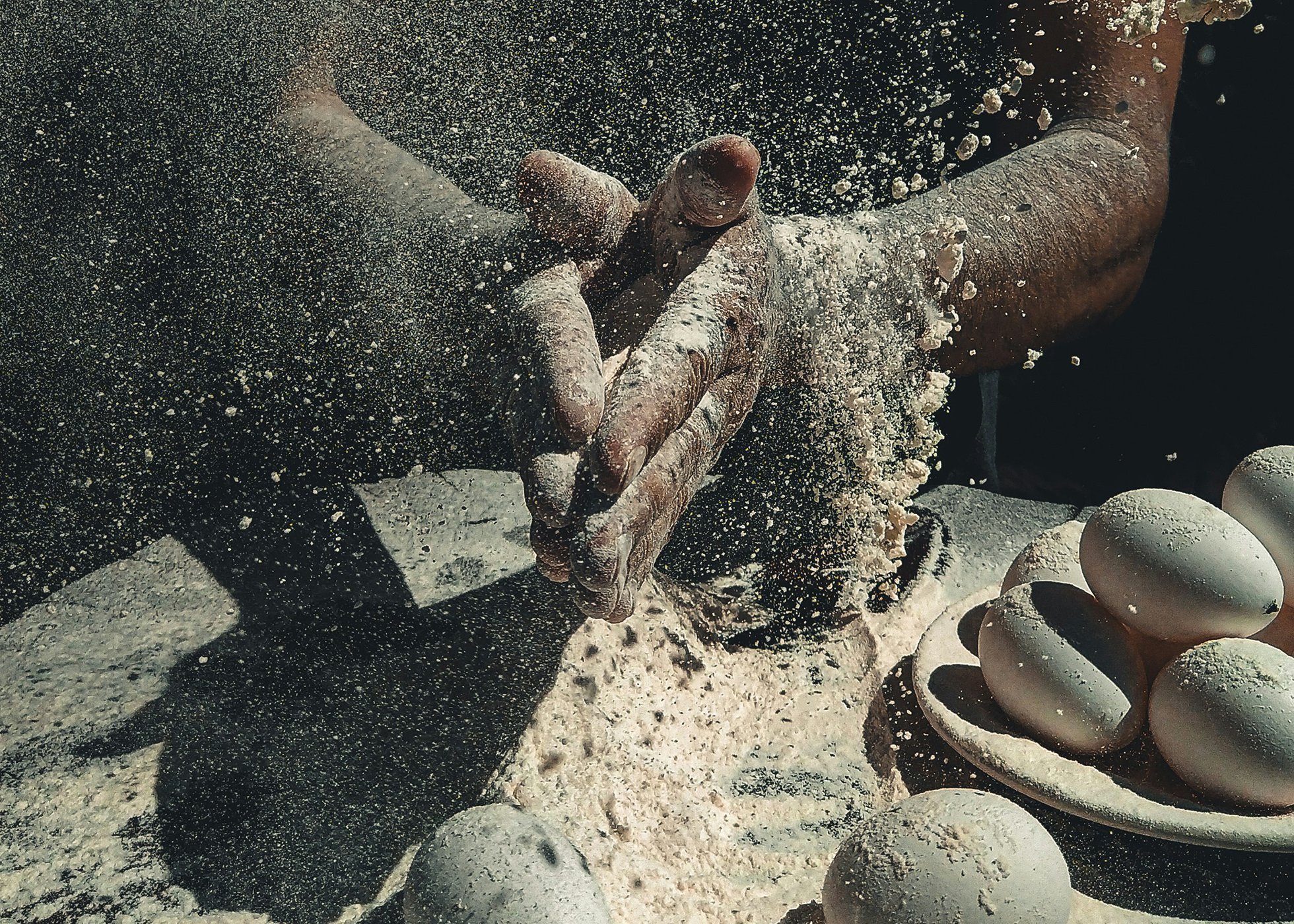 Cloud of flour as a baker claps their hands together while making food from flour & eggs