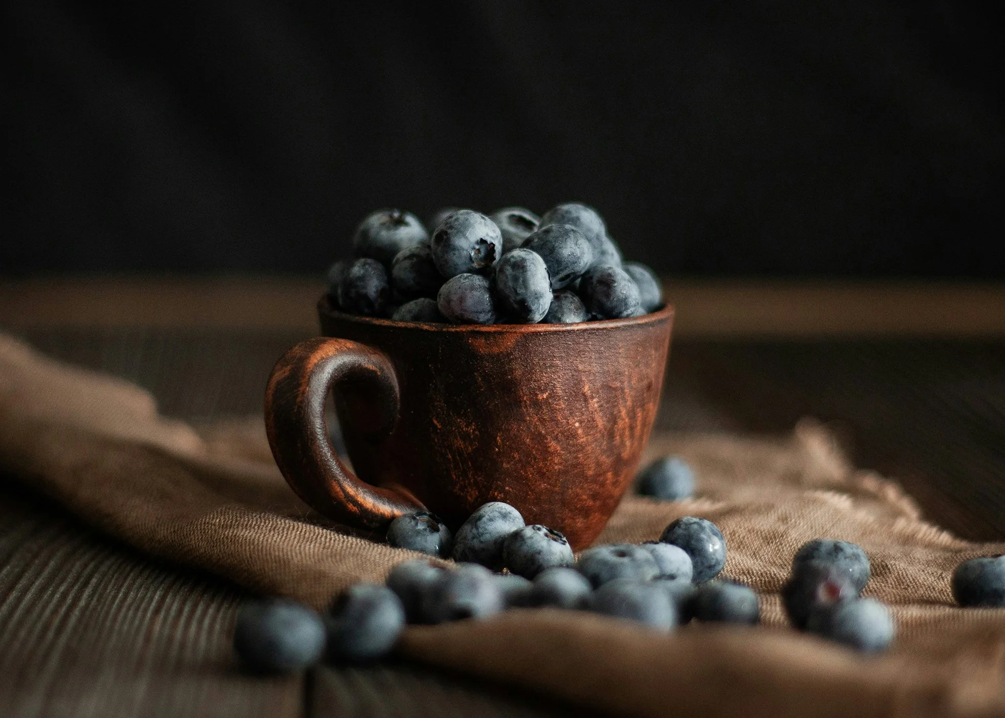 Cup filled with blueberries in a rustic kitchen table setting