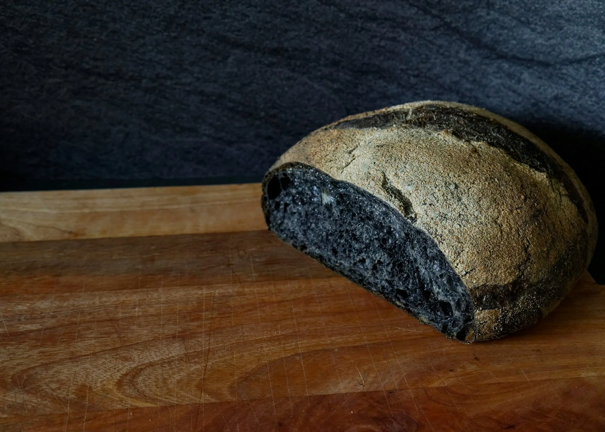 A loaf of very dark bread on a chopping board with a slice or two having been removed already