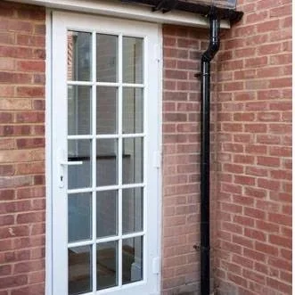 White exterior door with multiple glass panes next to a brick wall and black drainpipe.