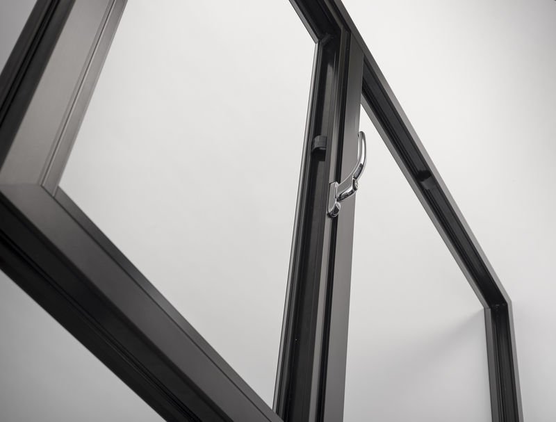 Close-up of a black window frame with a screen and a latch against a plain white wall.