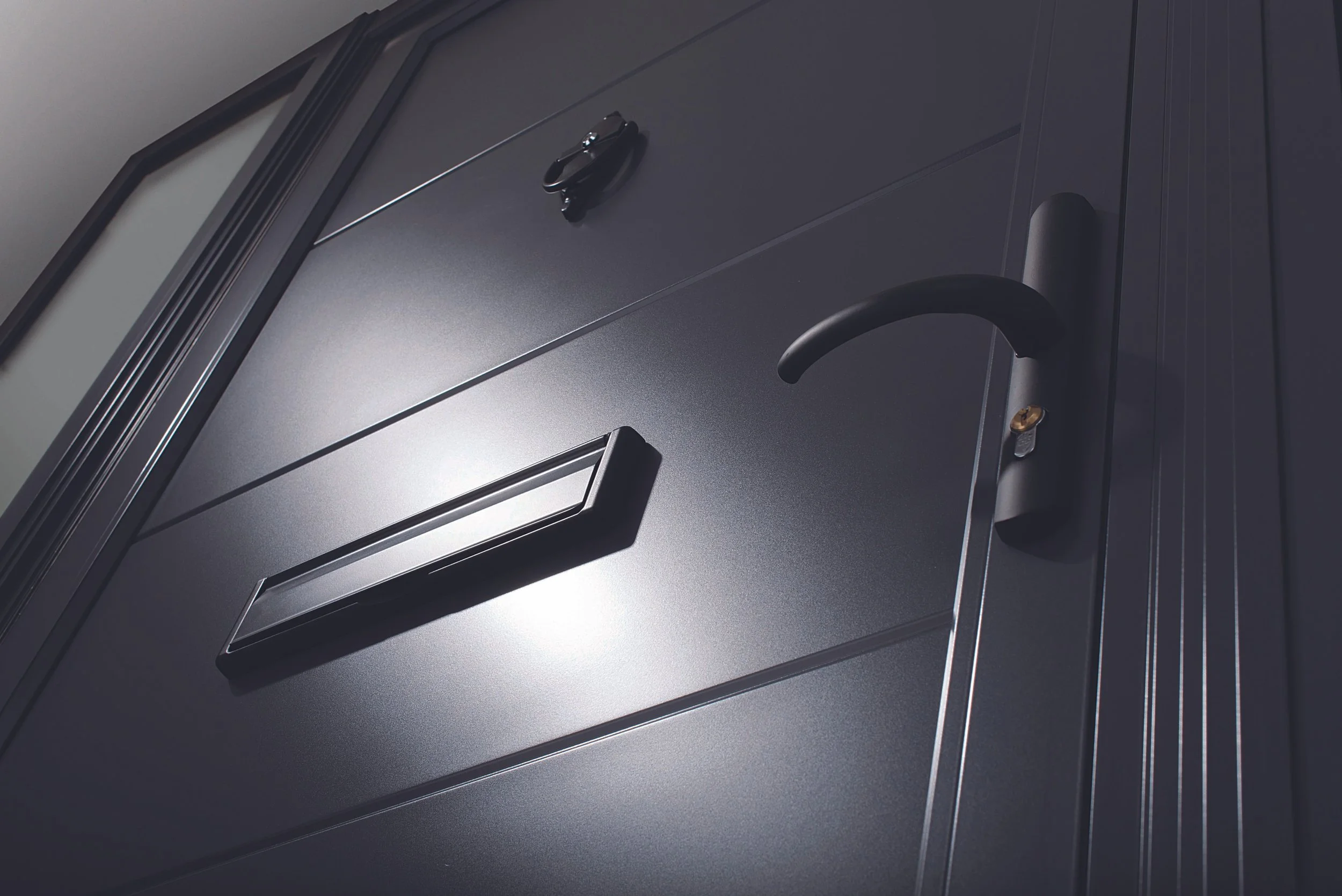 Close-up of a gray metal door with a black handle, mail slot, and a keyhole, viewed from an angle.