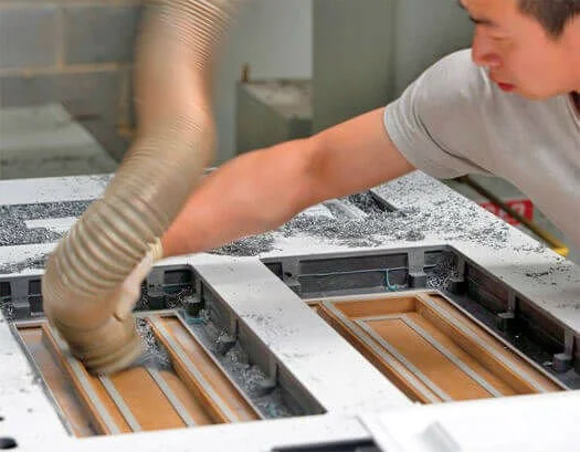 A man working on a large industrial machine or mold with a flexible hose above it in a workshop.