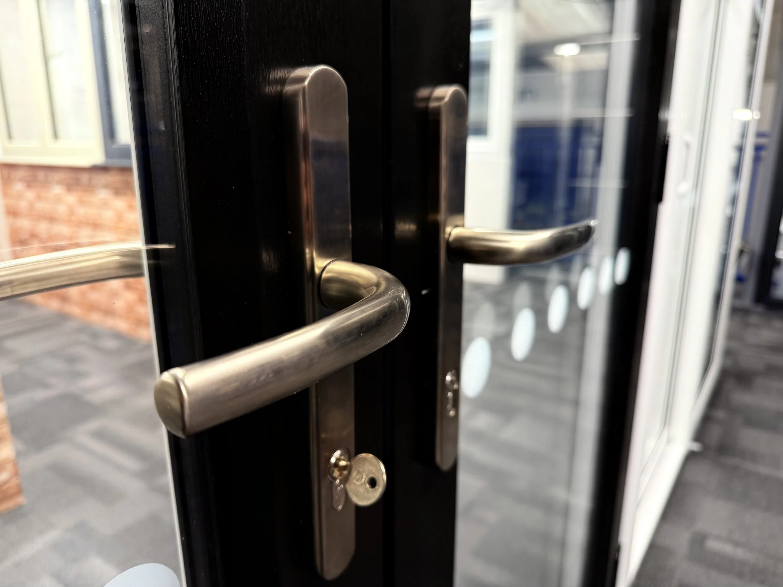Close-up of black glass double doors with metal handles and a key in the lock.