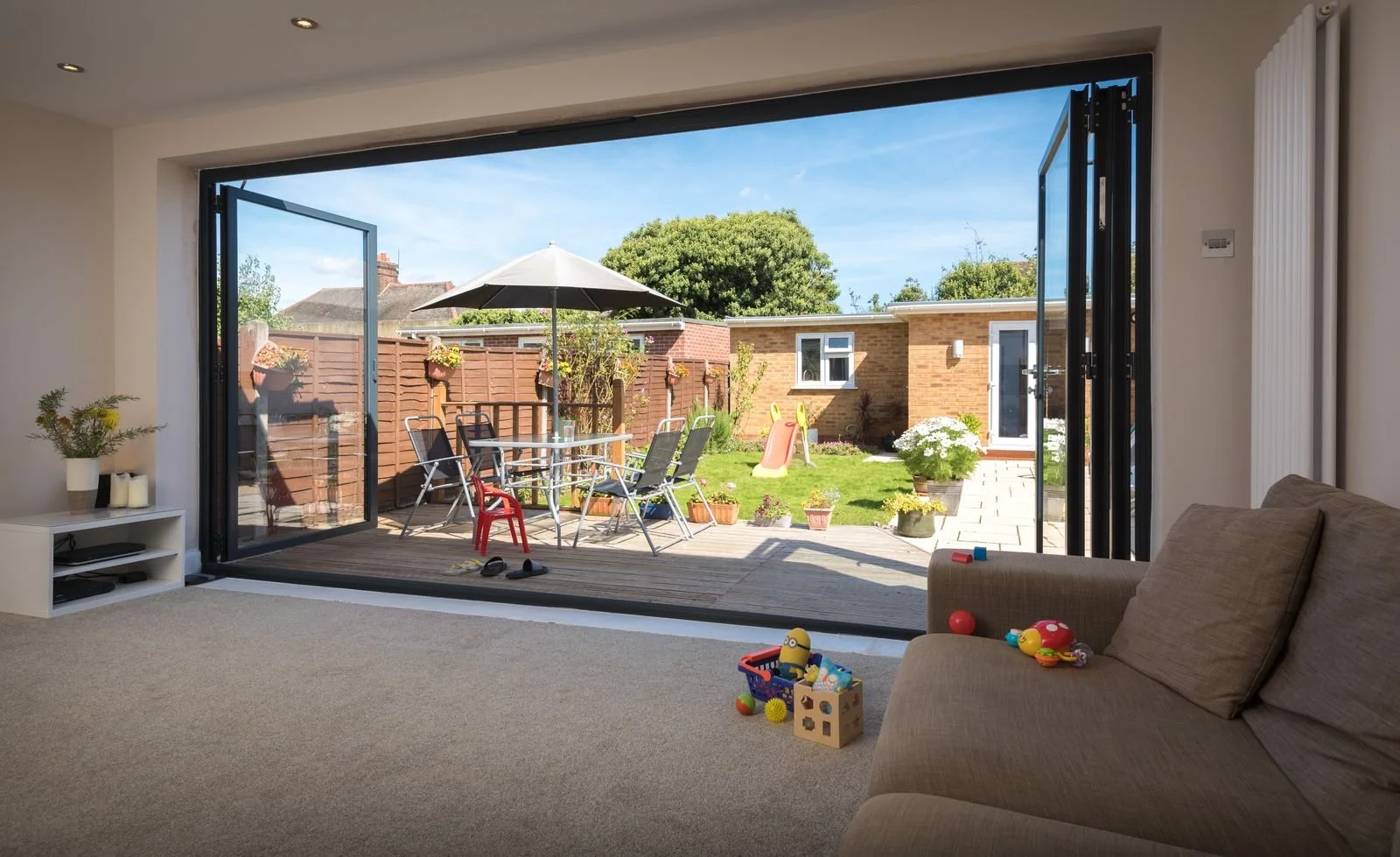 View from inside living room looking out to backyard with patio furniture, garden, and children's play equipment
