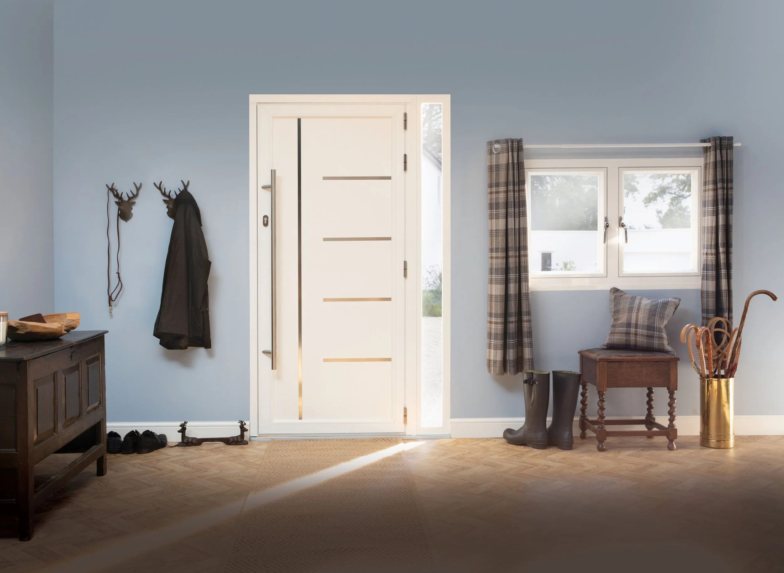 A bright entryway with a white modern front door, a small window, and winter boots. There's a wooden bench with a plaid pillow, a pair of black rubber boots, a gold container with walking sticks, and a wall hook with a coat and hat. The room has light blue walls and hardwood flooring.