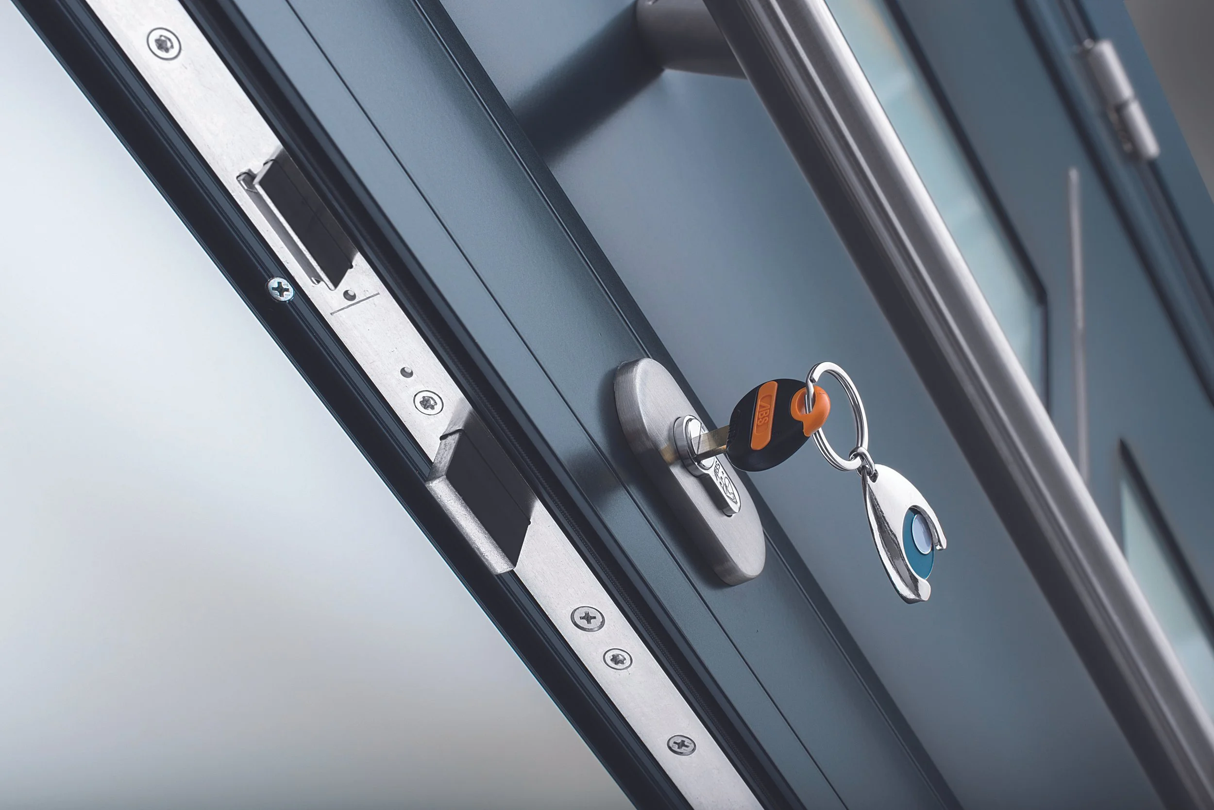 Close-up of a window with a key inserted into a lock, with a keychain attached, on a metal frame.