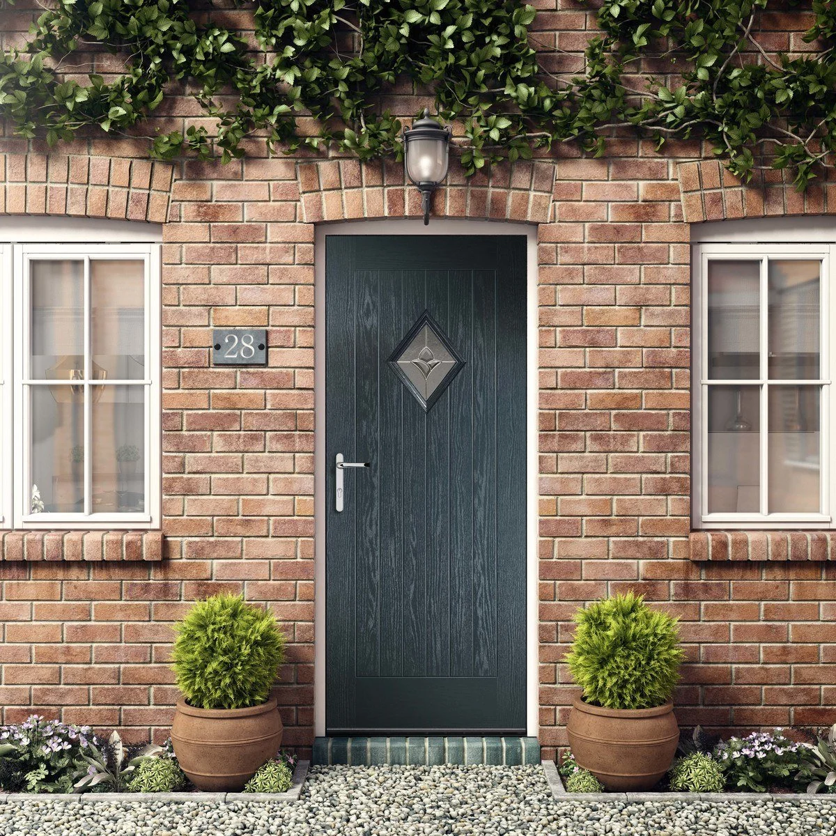 A brick house entrance with a dark door that has a diamond-shaped window, two white-paned windows on either side, potted plants, and a wall-mounted lantern above the door.