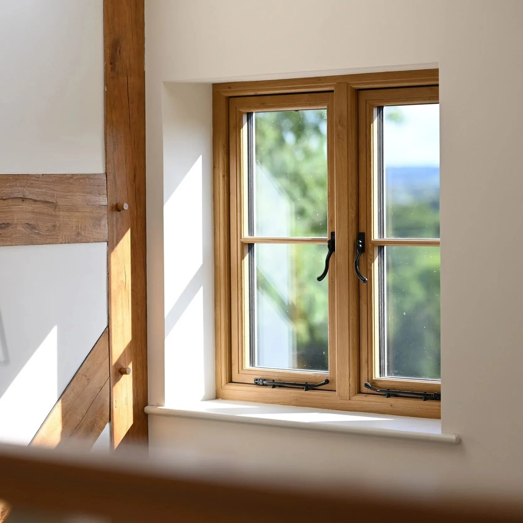 R9 PVC double-hung window with black handles, sunlight streaming through, and greenery outside