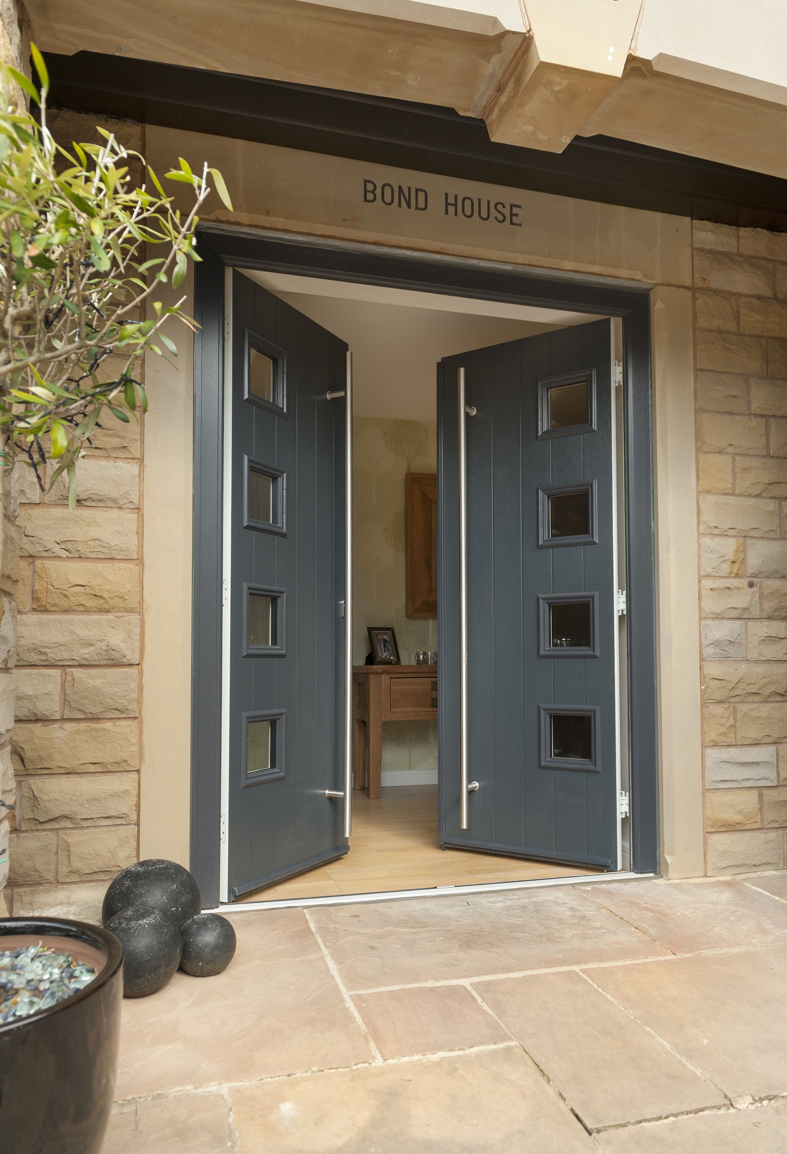 Open black front door with small square windows, leading into a house named 'Bond House'