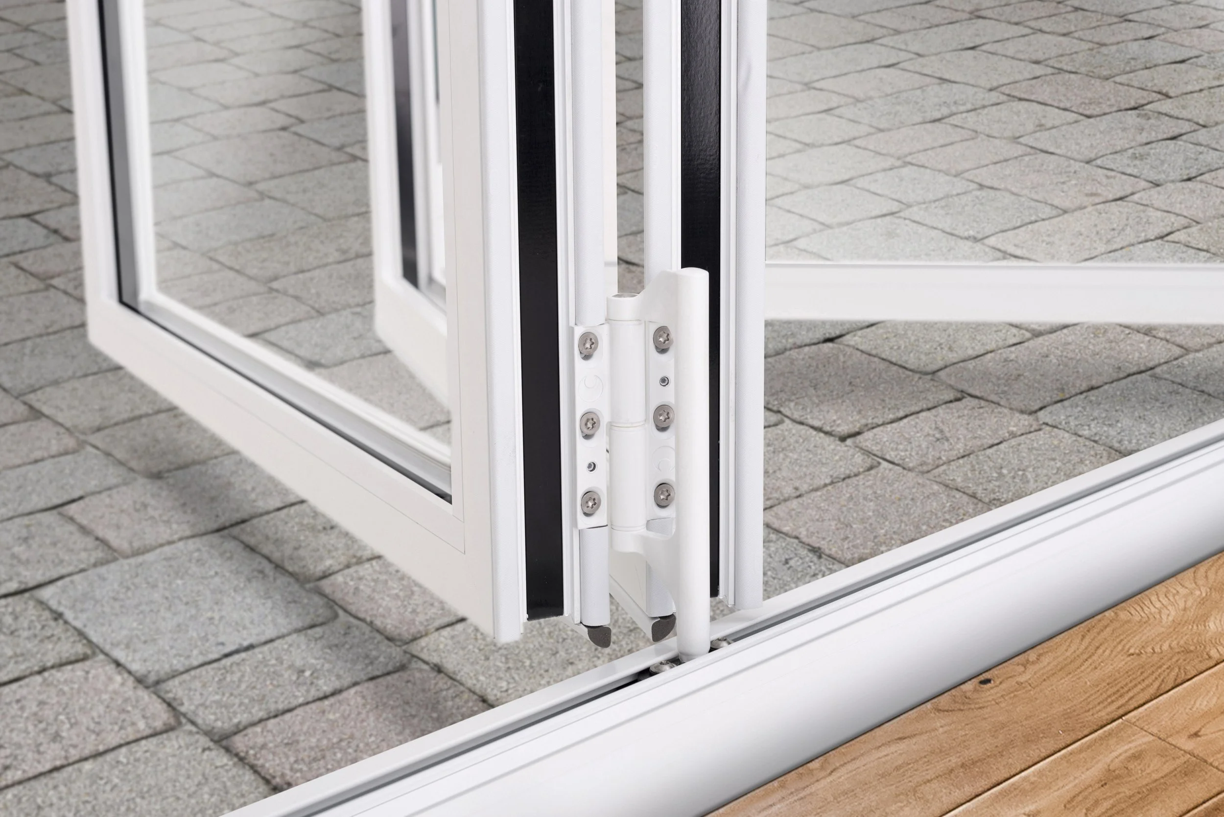 Close-up of a white sliding glass door hinge and frame, with a wooden floor and gray brick pavement outside.