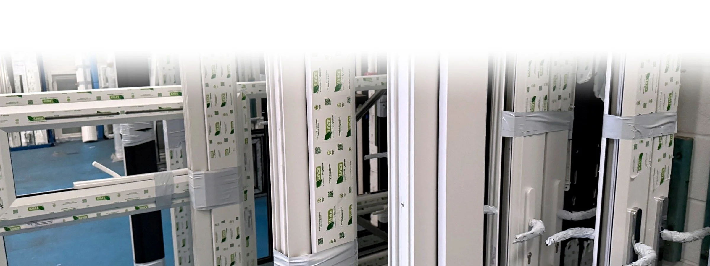 Propped-up windows framed in aluminum with protective film, stored in a warehouse.