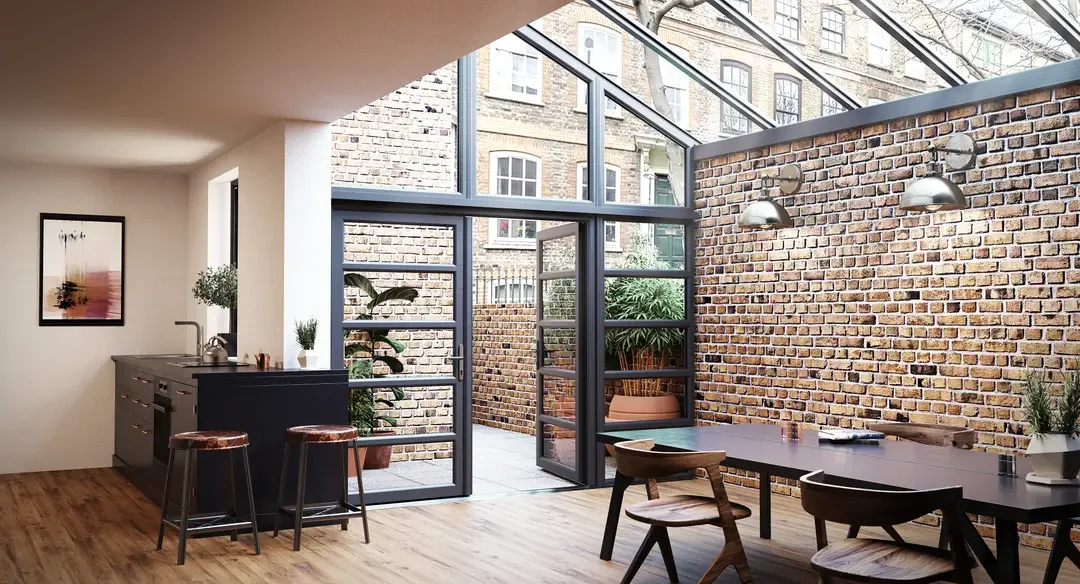 Modern indoor living space with a glass door leading to a brick patio, featuring a table with chairs, a small kitchen area, plants, and contemporary decor.