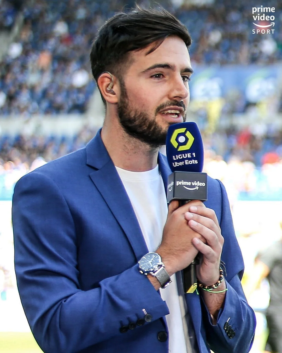 A man in a blue blazer holding a microphone with 'Ligue 1 Uber Eats' and 'Prime Video' logos during a sports broadcast