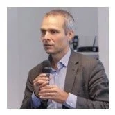 A man in a suit holding a microphone and speaking at an event.