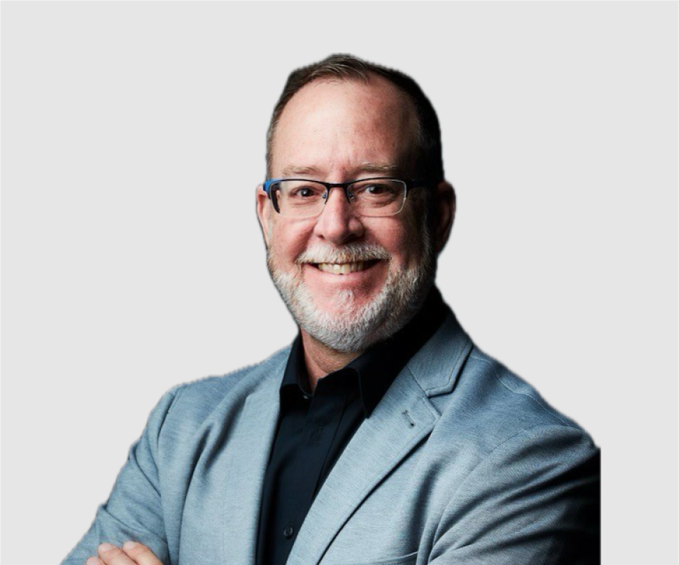 A smiling middle-aged man with glasses, a beard, and short hair, wearing a gray blazer and black shirt against a plain light background.