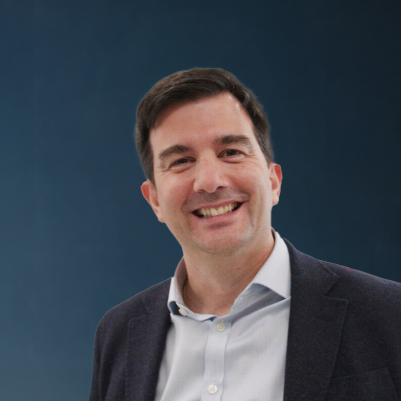 Portrait of a smiling man wearing a white shirt and blazer against a blue background.