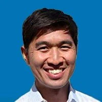 Portrait of a smiling man with dark hair against a blue background.