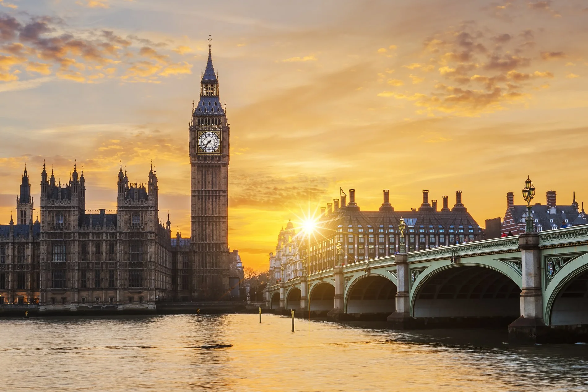 Sunset view of Big Ben and the Houses of Parliament in London, with the River Thames in the foreground and the Westminster Bridge to the right.