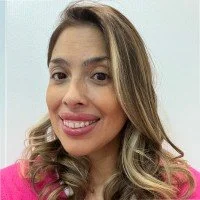 A woman smiling with long, wavy hair wearing a pink top.
