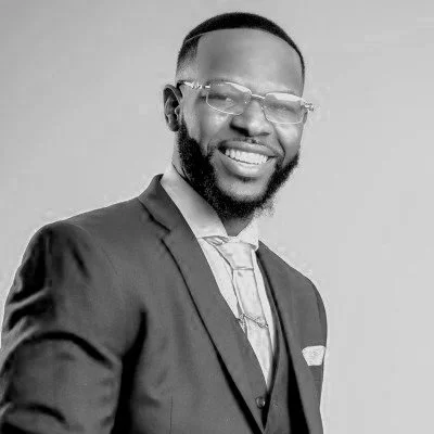 Black and white photo of a smiling man in a suit wearing glasses.