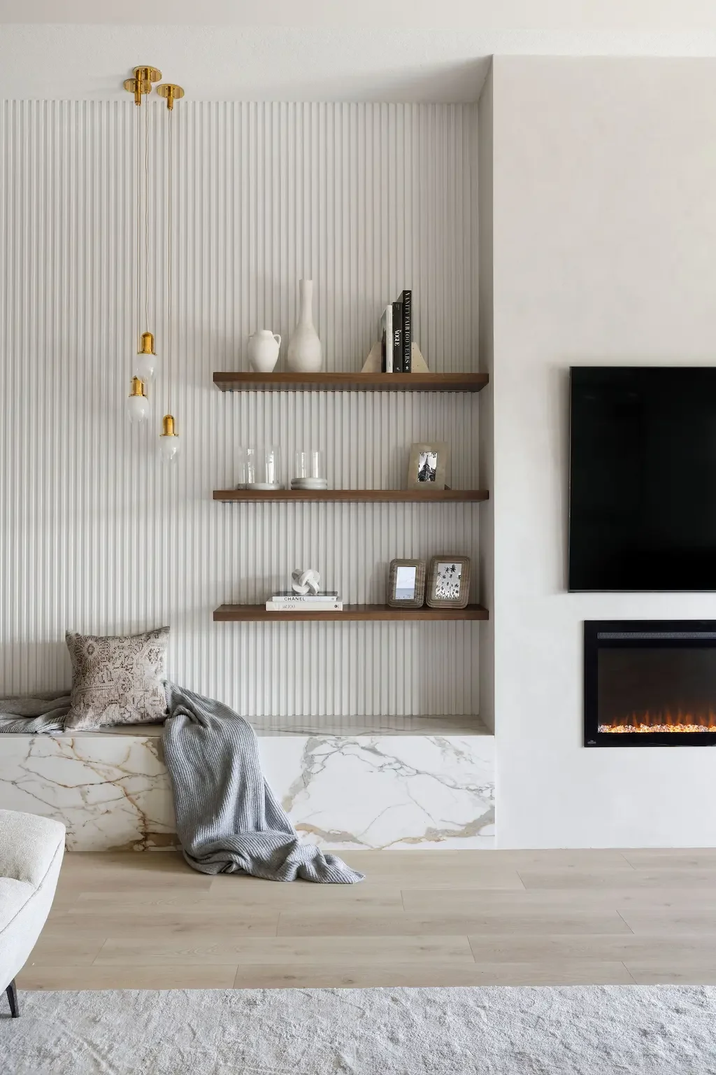 Luxury living room feature wall in Palm Beach Gardens FL with linear fireplace, fluted wall panels, floating shelves, and Calacatta marble bench by Interiors by Casa Mia.