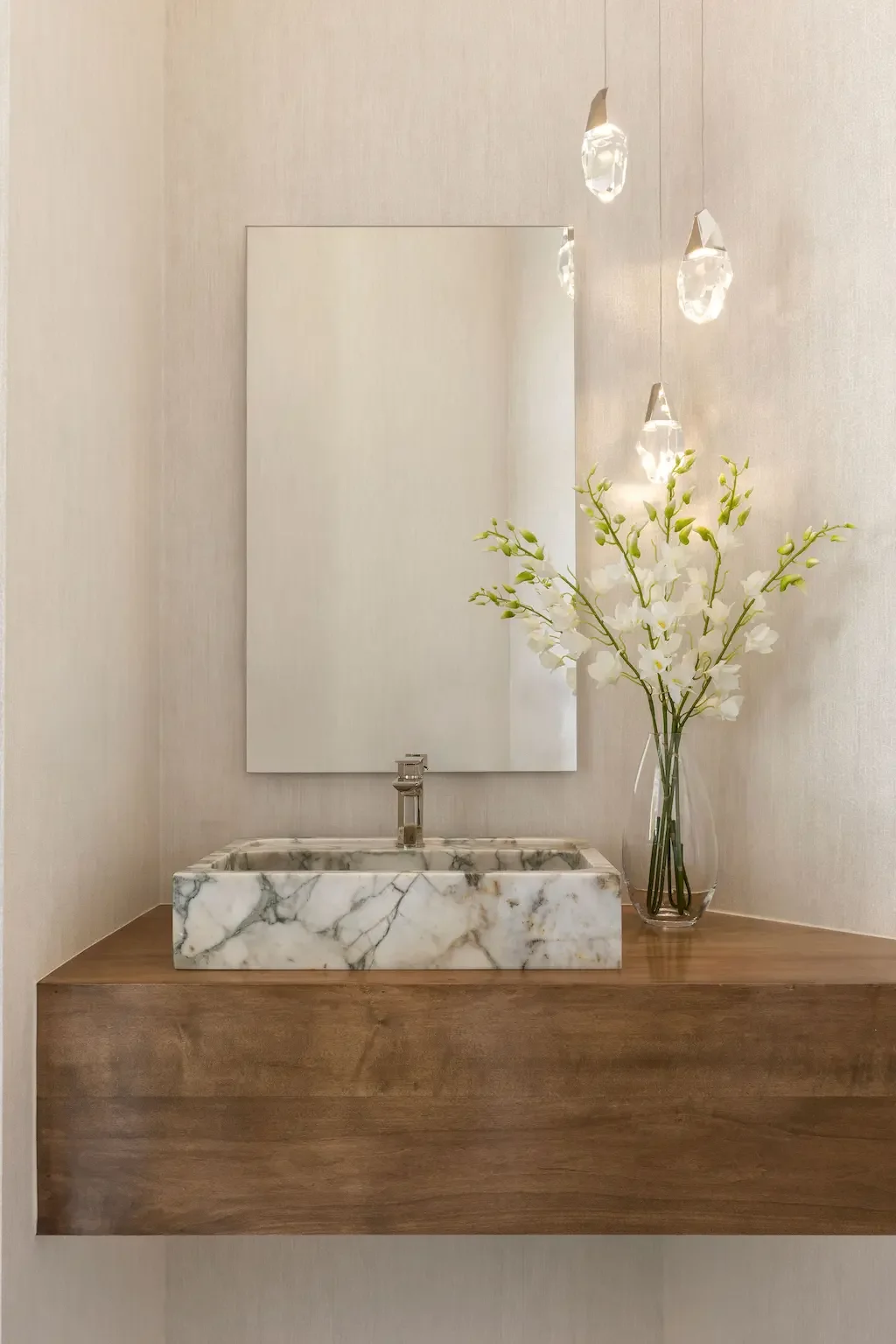 Luxury powder room interior design in Palm Beach Gardens FL with marble vessel sink, floating wood vanity, and crystal pendant lights by Interiors by Casa Mia.