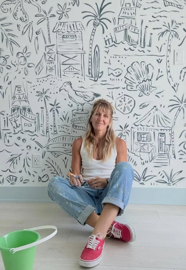 Jupiter FL artist Kourtney Cannon seated on the floor in front of her finished hand-painted vacation home mural, commissioned by interior designer Interiors by Casa Mia
