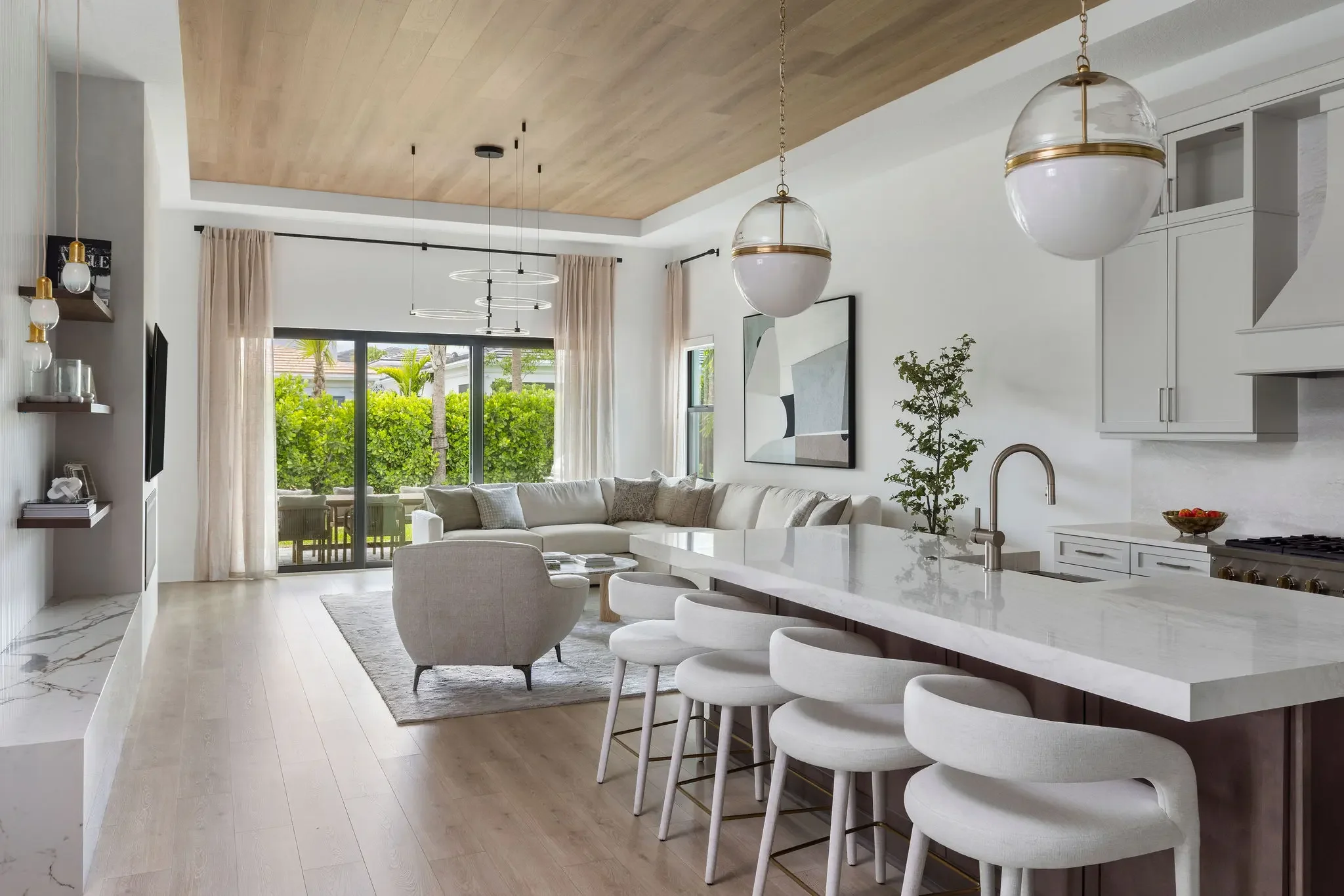 Modern living room and kitchen in Palm Beach Gardens FL with custom wood ceiling, stone fireplace, and full furnishing by Interiors by Casa Mia.
