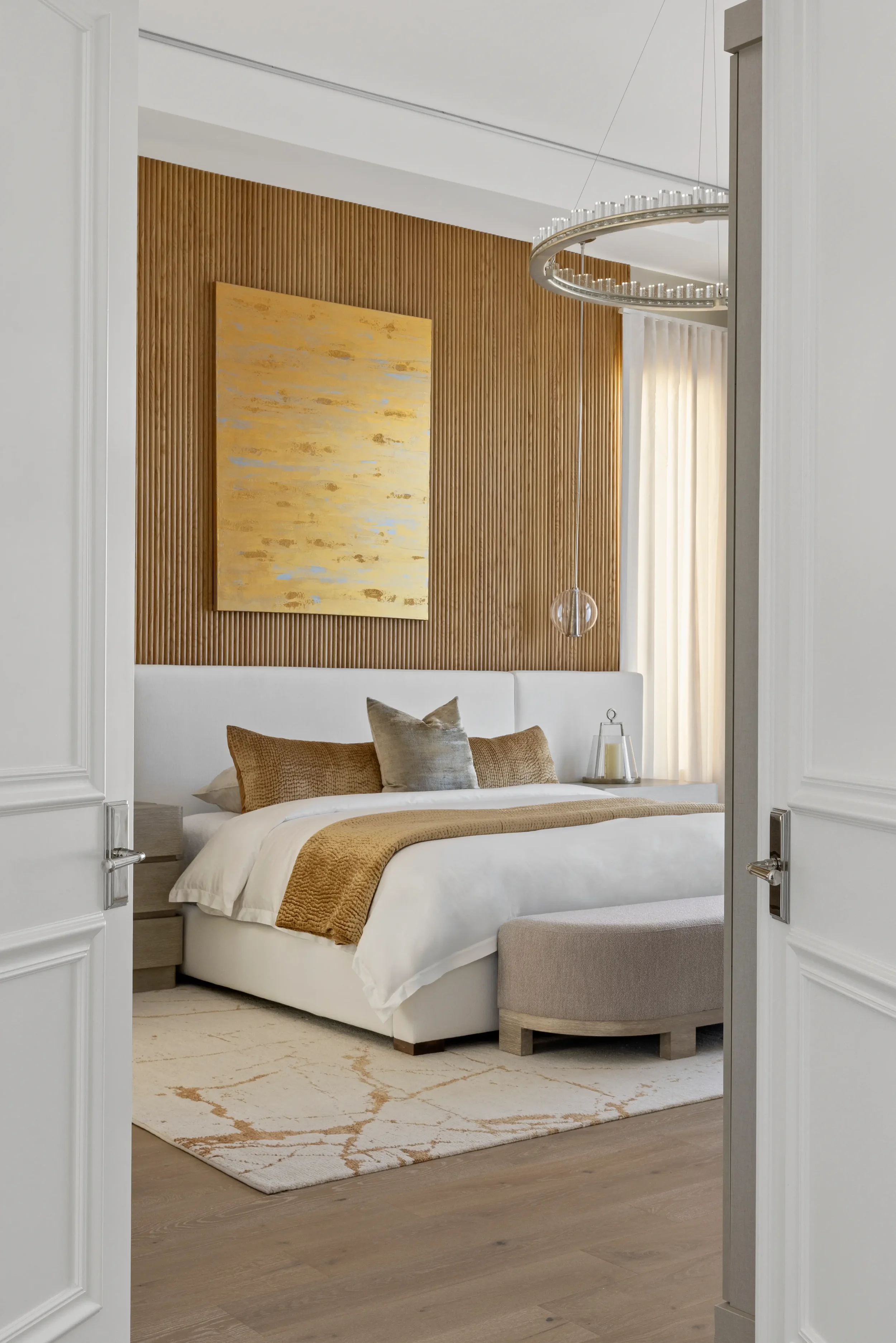 Luxury primary bedroom with wood accent wall and statement chandelier — design by Interiors by Casa Mia, Jupiter FL