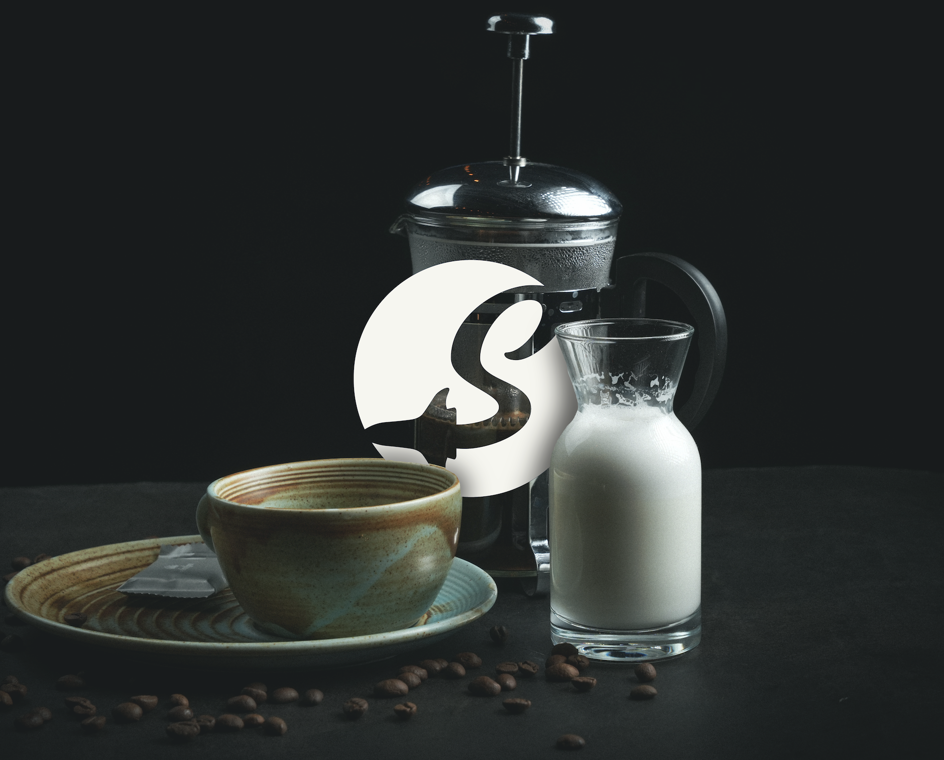 A glass jar of coffee with a lid and a plunger, a glass pitcher of milk, and a ceramic cup with a matching saucer on a dark surface, surrounded by scattered coffee beans.
