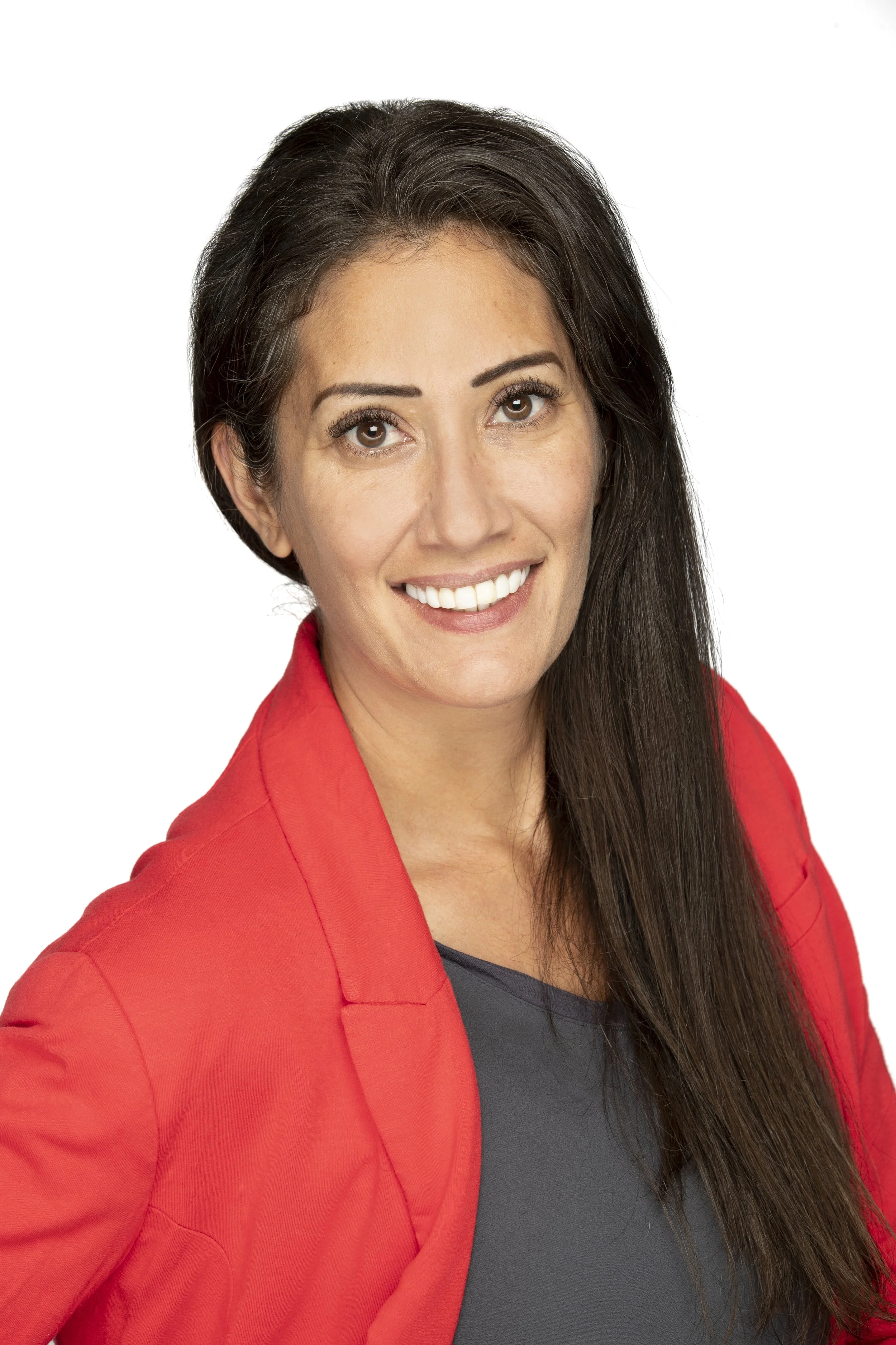 A woman smiling, wearing a red blazer and a dark top, with long dark hair, against a white background.