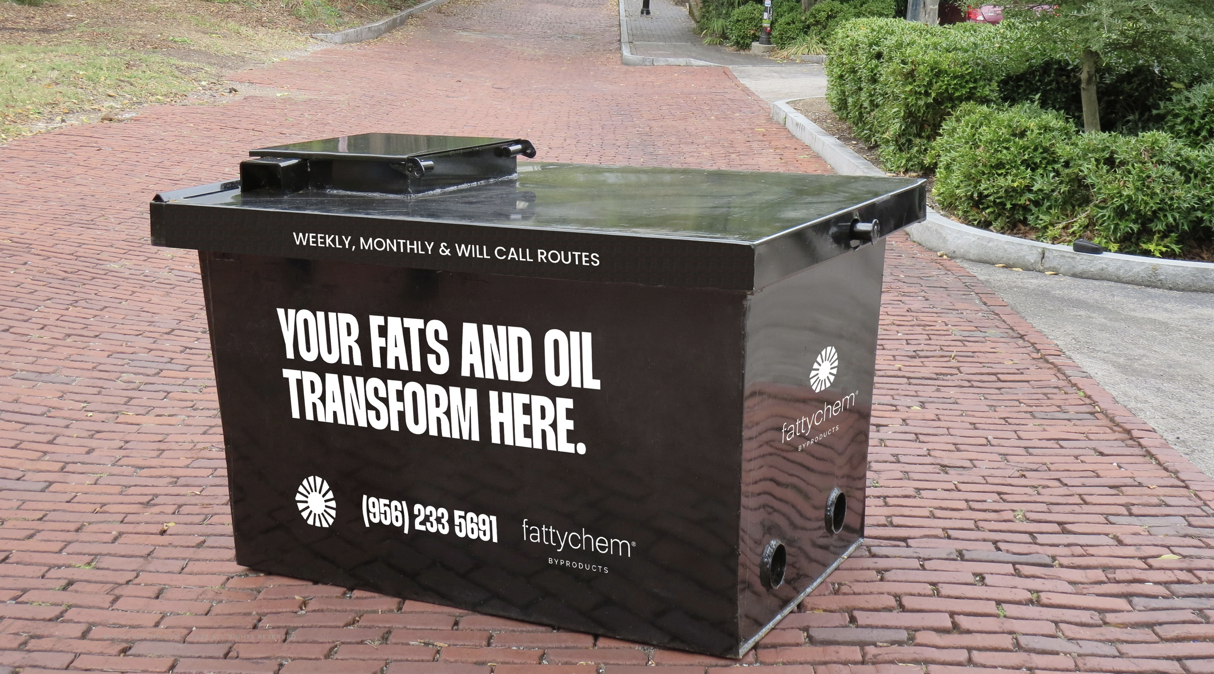 Fatty Chem branded outdoor used cooking oil recycling container labeled ‘Your Fats and Oil Transform Here,’ placed on a brick pathway with greenery in the background.