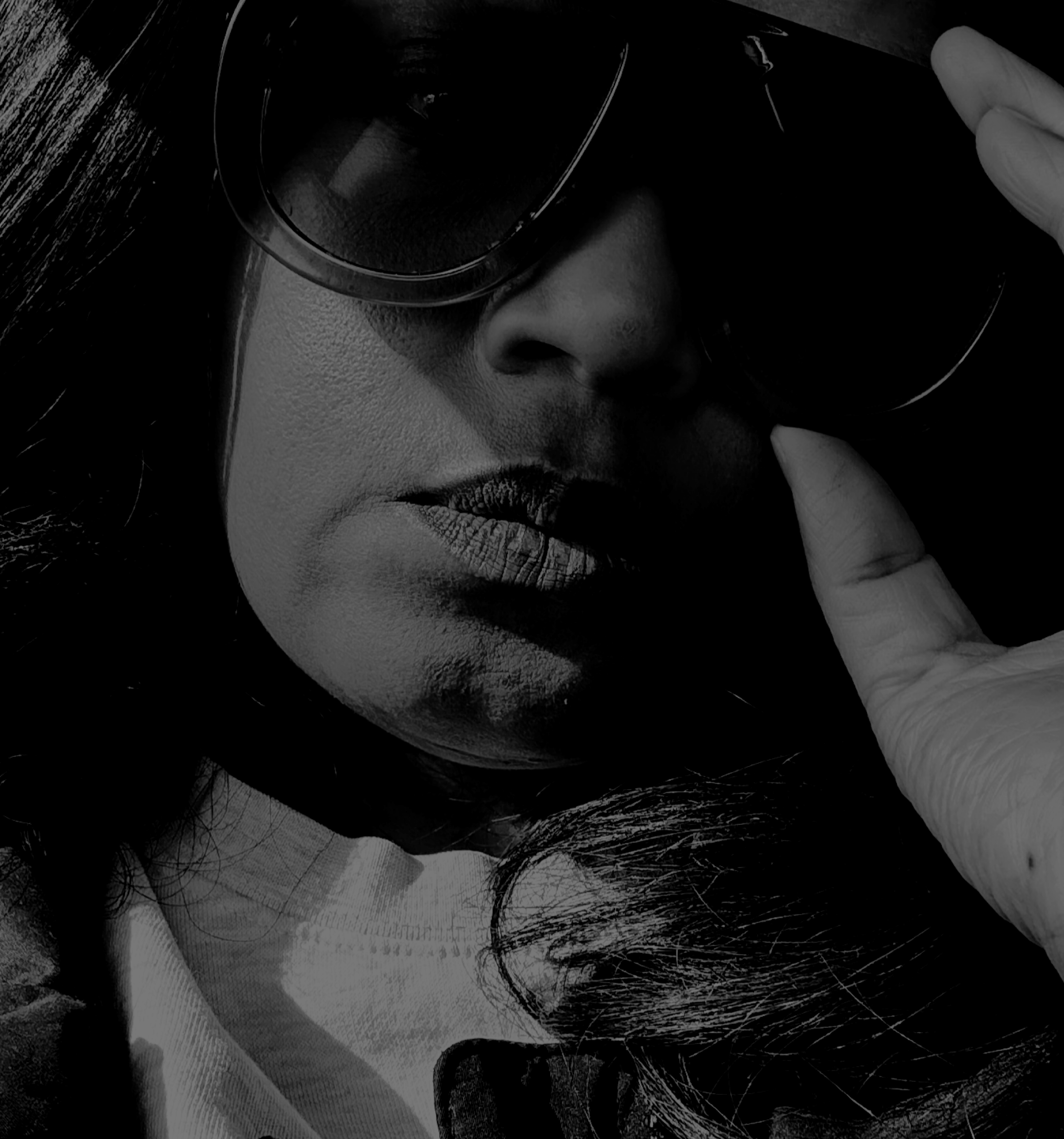 Black and white close-up of a woman with long, dark hair wearing glasses, touching her forehead gently with her hand.