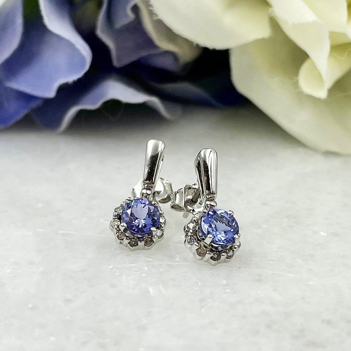 close up in front of flowers Tanzanite With Diamond Halo Drop Stud Earrings 14k White Gold