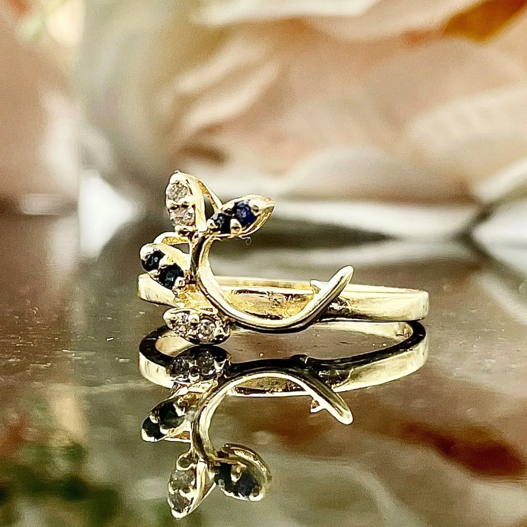 close up of 14k Yellow Gold Sapphire And Diamond Leaf Wrap Wedding Band in front of flowers