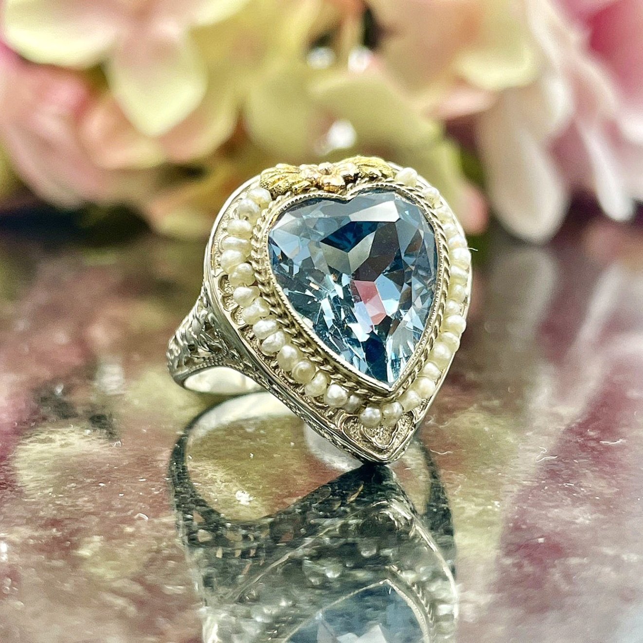 3/4 close up in front of flowers Vintage 14k White Gold Blue Topaz Heart With Seed Pearls Ladies Ring