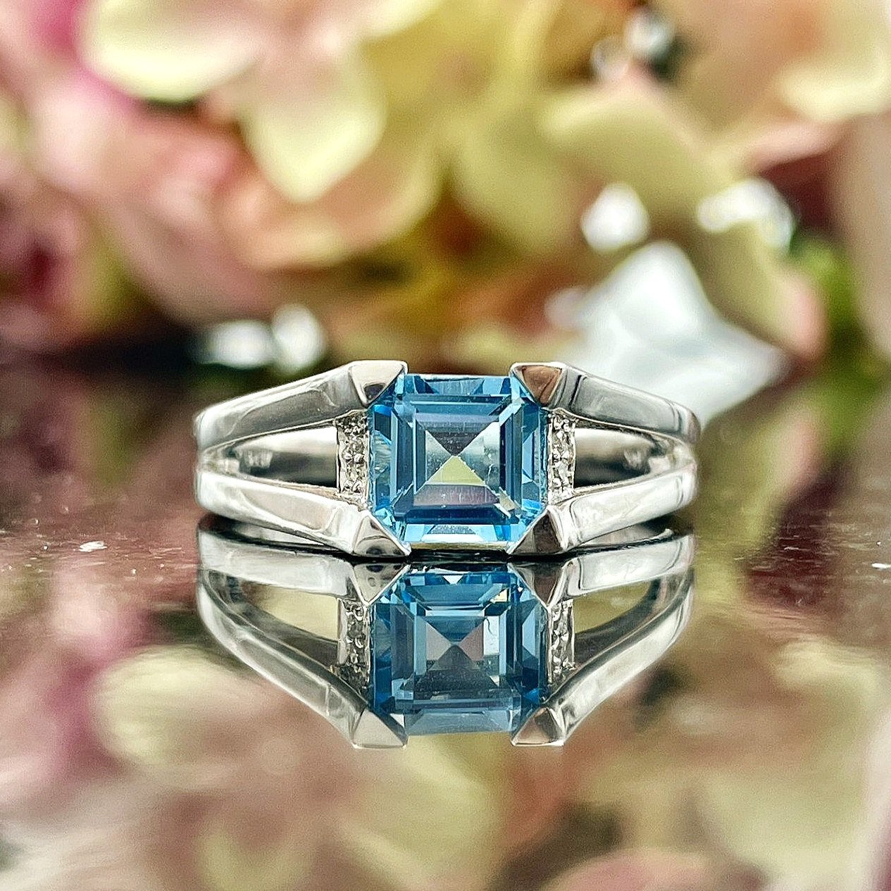 close up in front of flowers 14k White Gold Blue Topaz And Diamond Split Shoulder Ring