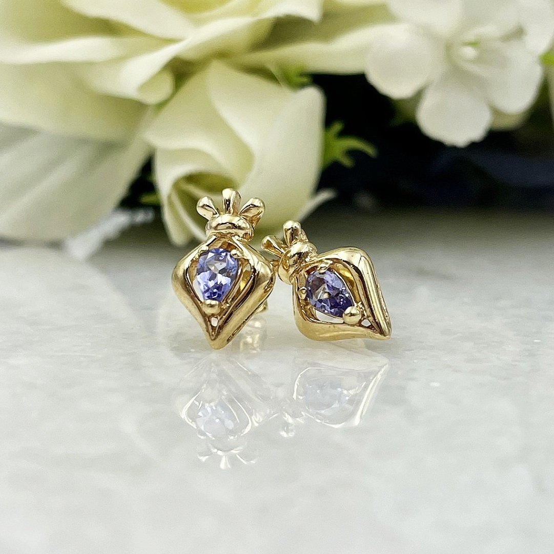 Tanzanite Stud Earrings Framed in Unique 14K Yellow Gold Setting in front of flowers