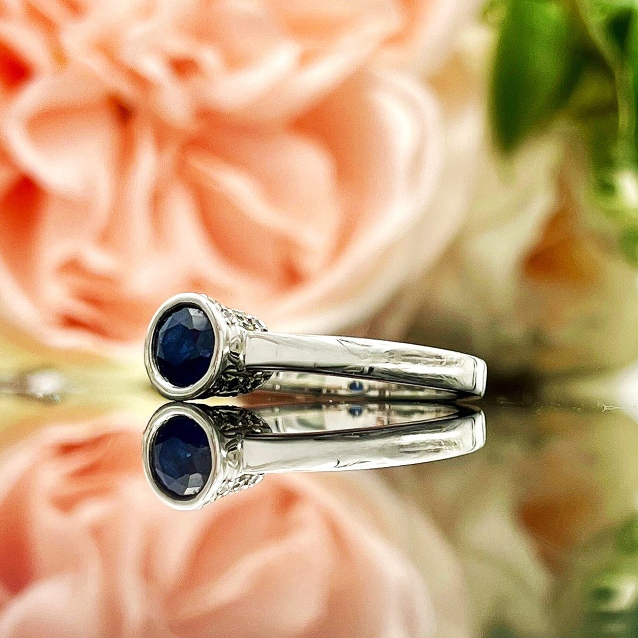 close up in front of flowers 14k White Gold Bezel Set Sapphire With Peekaboo Diamonds Ladies Ring