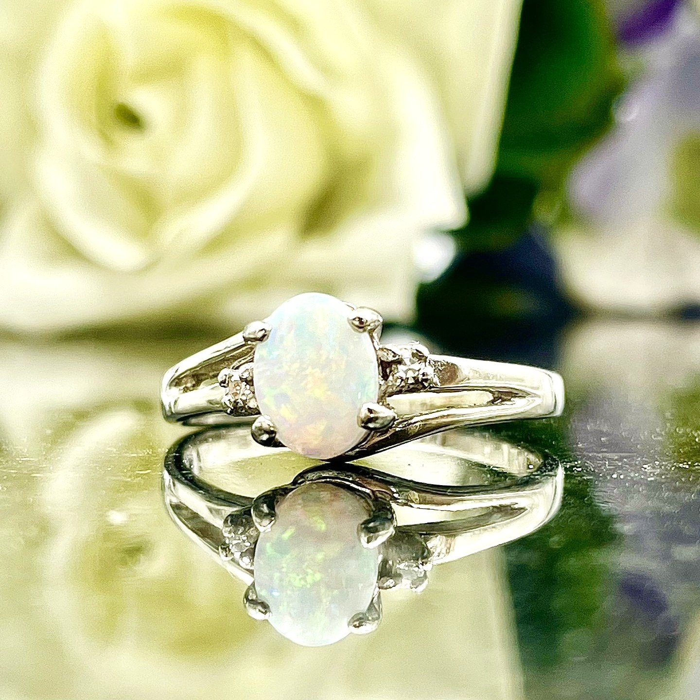 close up in front of flowers 10k White Gold Oval Opal With Diamond Accents Three Stone Ring