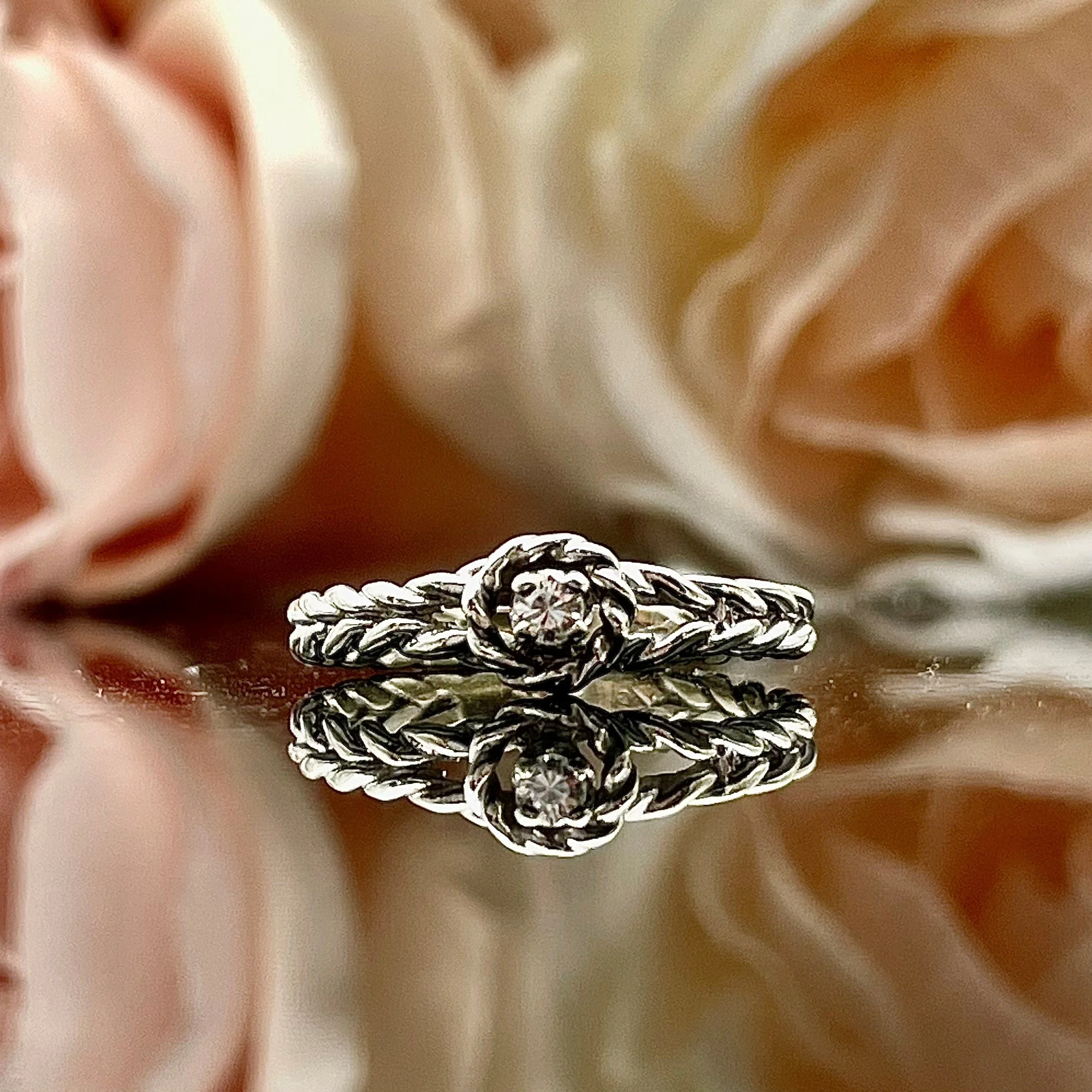 close up of rope patterned 14k white gold promise ring with diamond in front of pink florals