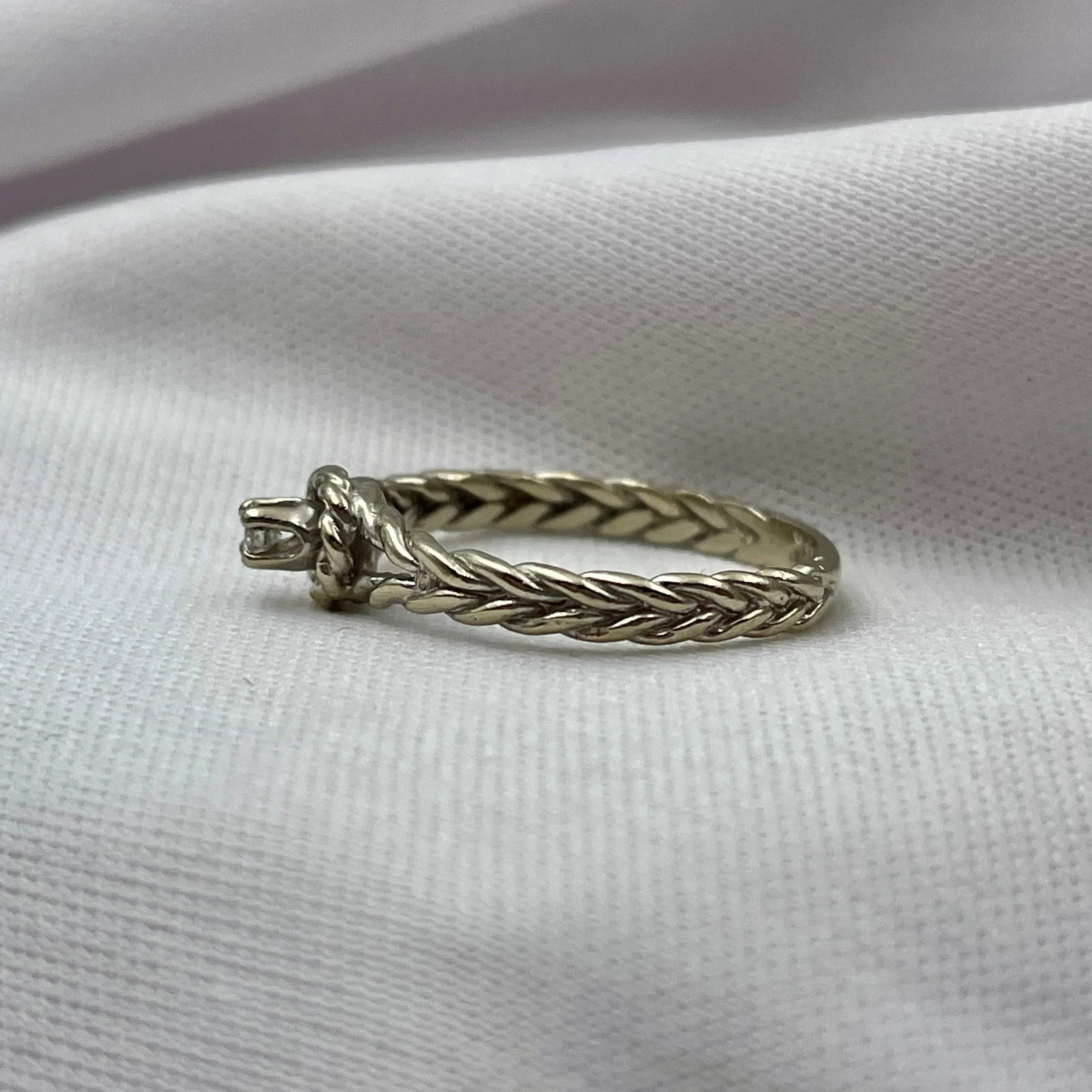side view of white gold rope patterned diamond promise ring with white fabric background