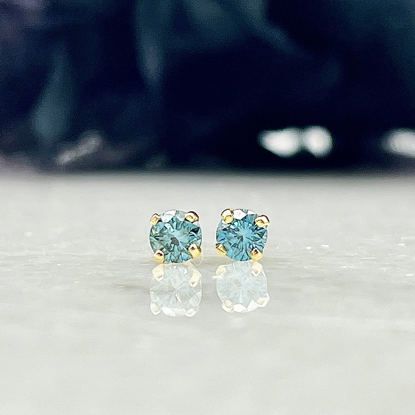 close up in front of florals .28ctw Treated Blue Diamond Stud Earrings 14k Yellow Gold