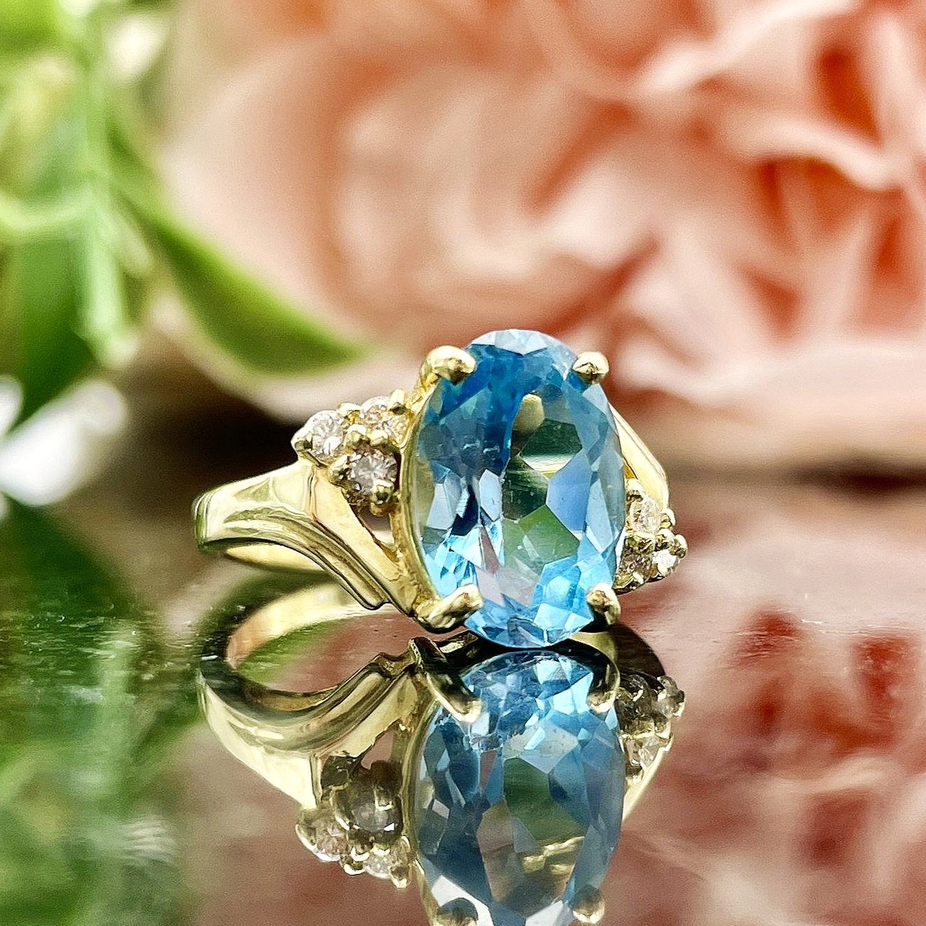 close up in front of flowers 14k Yellow Gold Oval Cut Blue Topaz With Diamond Accents Ladies Bypass Ring